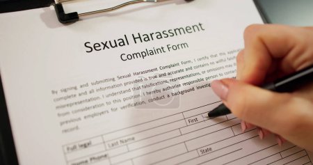 Foto de Primer plano de una mano humana llenando formulario de queja de acoso sexual con pluma - Imagen libre de derechos