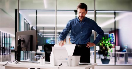 Téléchargez les photos : Homme d'affaires irrité regardant du papier coincé dans l'imprimante au bureau - en image libre de droit