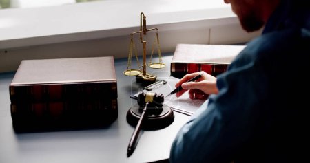 Photo for Close-up Of Judge Holding Document With Gavel At Desk - Royalty Free Image