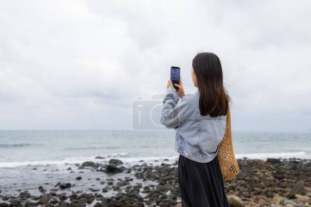 Téléchargez les photos : Femme prendre des photos avec téléphone portable de la plage de la mer - en image libre de droit