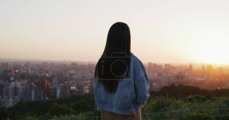 Téléchargez les photos : Vue arrière de la femme regarder la ville sous le coucher du soleil - en image libre de droit