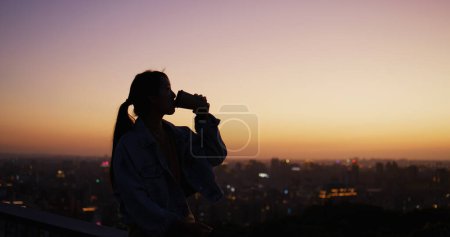 Téléchargez les photos : Femme profiter de son café chaud et regarder la vue sur le coucher du soleil - en image libre de droit