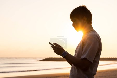 Foto de Silueta del hombre utilizar el teléfono móvil al atardecer en la playa - Imagen libre de derechos
