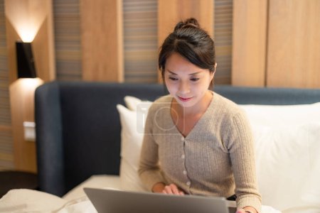 Téléchargez les photos : Femme travail sur ordinateur portable et s'asseoir sur le lit la nuit - en image libre de droit