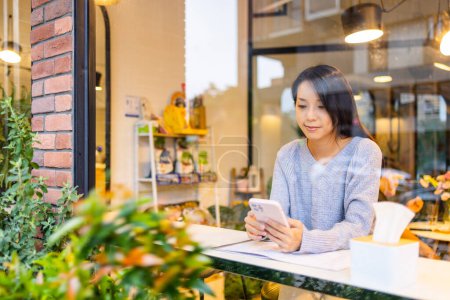 Téléchargez les photos : Femme utilisation de téléphone portable dans le café avec reflet de fenêtre - en image libre de droit