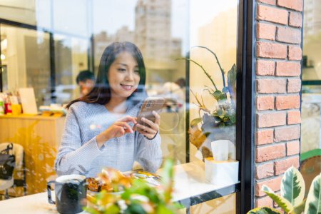 Téléchargez les photos : Femme utilisation de téléphone portable dans le café avec reflet de fenêtre - en image libre de droit