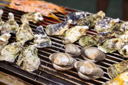 Téléchargez les photos : Grill huîtres palourdes et crevettes sur filet métallique dans le marché de rue - en image libre de droit