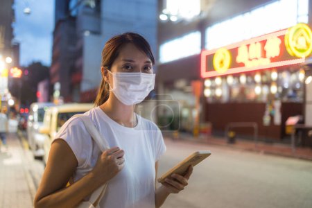 Téléchargez les photos : Femme porter un masque facial et utiliser un téléphone mobile dans la ville la nuit - en image libre de droit