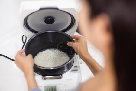 Téléchargez les photos : Femme se préparer à cuire le riz Jasmine dans une cuisinière à riz électrique - en image libre de droit