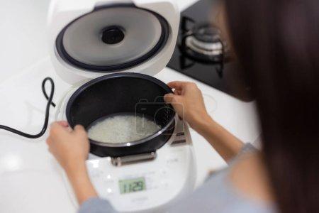 Foto de Mujer prepararse para cocinar arroz jazmín en olla de arroz eléctrico - Imagen libre de derechos