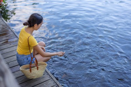Téléchargez les photos : Voyage femme nourrir le poisson carpe dans l'étang d'eau - en image libre de droit