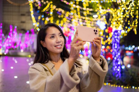 Téléchargez les photos : Femme utiliser un téléphone mobile pour prendre des photos avec décoration de lumière de Noël - en image libre de droit