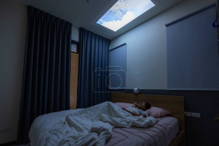Photo for Woman lying down on bed and watch the video project on the ceiling at home - Royalty Free Image