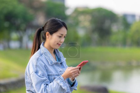 Téléchargez les photos : Femme vérifier sur téléphone portable au parc - en image libre de droit