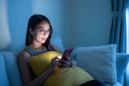 Téléchargez les photos : Femme avec des lunettes et l'utilisation du téléphone intelligent à la maison le soir - en image libre de droit