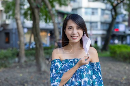Photo for Woman take off the face mask and smile to camera in city - Royalty Free Image
