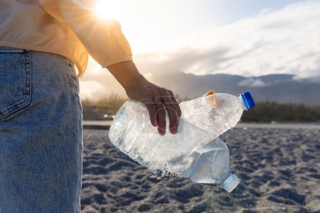 Foto de Mujer recogiendo a mano botella de plástico de limpieza en la playa - Imagen libre de derechos