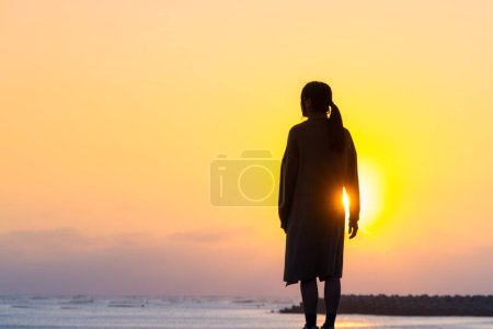 Téléchargez les photos : Silhouette de femme debout au coucher du soleil sur la plage - en image libre de droit