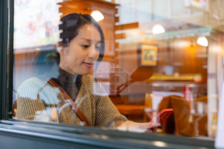 Téléchargez les photos : Femme regarder à l'extérieur de la fenêtre à l'intérieur du café et l'utilisation du téléphone mobile - en image libre de droit