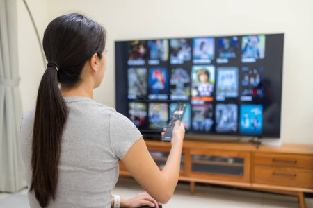 Foto de Mujer ver la televisión y el uso de control remoto para elegir el programa en casa - Imagen libre de derechos