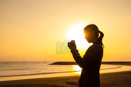 Téléchargez les photos : Lady silhouette avec appareil photo pour prendre des photos à la plage en bord de mer - en image libre de droit