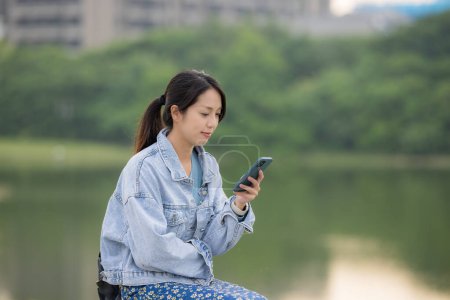 Téléchargez les photos : Jeune femme regarder téléphone mobile au bord du lac - en image libre de droit