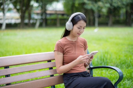Téléchargez les photos : Femme écouter casque avec téléphone portable au parc - en image libre de droit