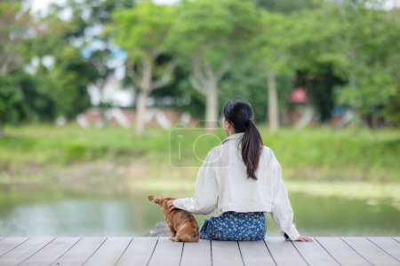 Foto de Mujer sentada con su perro salchicha al lado del lago en el parque - Imagen libre de derechos