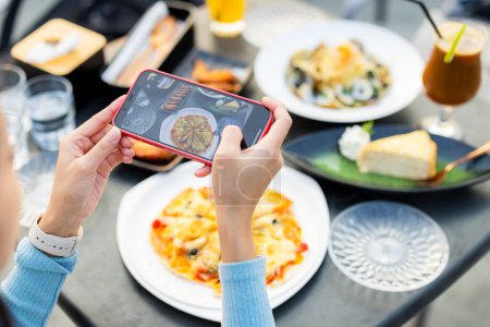 Téléchargez les photos : Téléphone portable femme pour prendre des photos sur la nourriture au restaurant - en image libre de droit