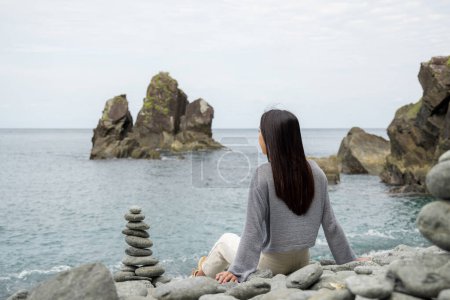 Foto de Mujer sentada en la playa de piedra - Imagen libre de derechos