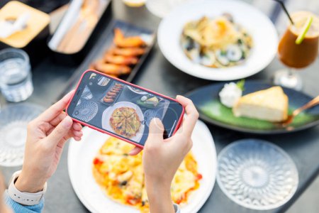 Téléchargez les photos : Téléphone portable femme pour prendre des photos sur la nourriture au restaurant - en image libre de droit