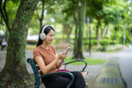 Téléchargez les photos : Femme écouter sur le casque et s'asseoir à l'intérieur du parc - en image libre de droit