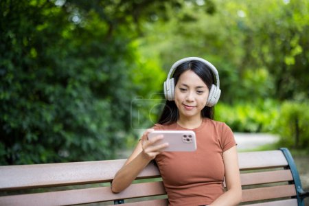 Téléchargez les photos : Femme regarder sur téléphone mobile et s'asseoir au parc - en image libre de droit