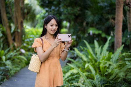 Téléchargez les photos : Femme utiliser un téléphone portable pour prendre des photos dans le parc - en image libre de droit