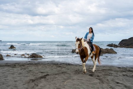 Téléchargez les photos : Femme touristique monter à cheval à côté de la plage de la mer - en image libre de droit