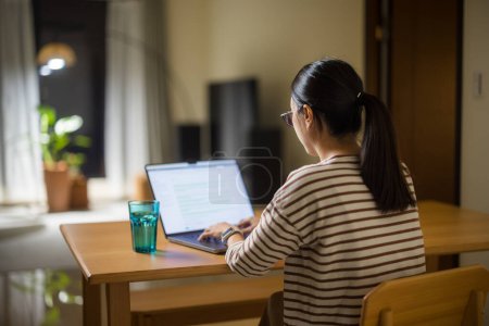 Téléchargez les photos : Femme formulaire de travail à la maison avec ordinateur portable dans la soirée - en image libre de droit