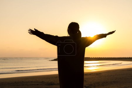 Téléchargez les photos : Silhouette de femme debout au coucher du soleil sur la plage avec bras ouvert - en image libre de droit