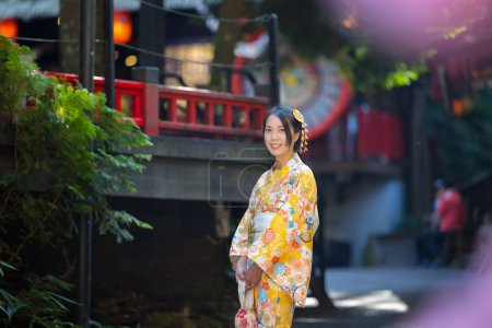 Téléchargez les photos : Femme asiatique essayer de porter kimono japonais avec l'arrière-plan traditionnel du village japonais - en image libre de droit
