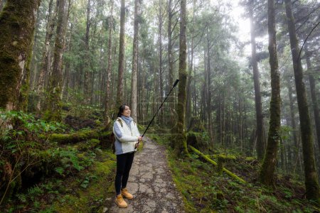 Téléchargez les photos : Femme utiliser un appareil photo pour faire une promenade photo dans la forêt brumeuse brumeuse à Taipingshan Jianqing Huaigu Trail - en image libre de droit