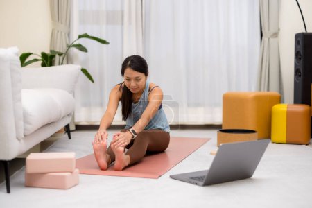 Téléchargez les photos : Femme à la maison faire de l'exercice de yoga avec son ordinateur portable - en image libre de droit