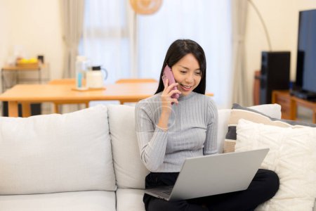 Woman work on laptop computer and talk to cellphone at home