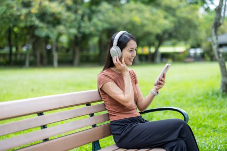 Téléchargez les photos : Femme écouter de la musique et utiliser un téléphone portable au parc - en image libre de droit