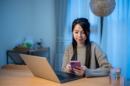 Téléchargez les photos : Femme utiliser ordinateur portable avec utilisation de téléphone portable à la maison - en image libre de droit