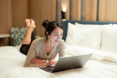 Téléchargez les photos : Femme montre sur ordinateur portable et couché sur le lit à la maison - en image libre de droit