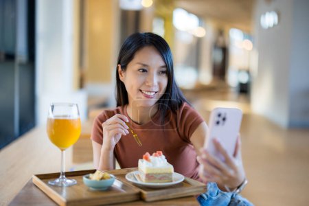 Téléchargez les photos : Femme prendre selfie sur téléphone portable avec le thé de l'après-midi dans le café - en image libre de droit
