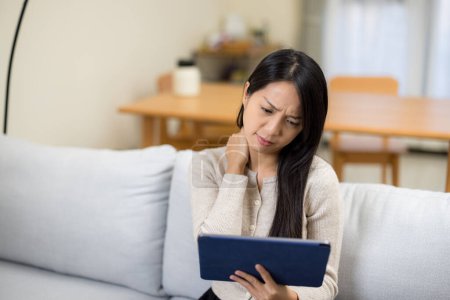 Téléchargez les photos : Femme souffrent de douleurs au cou et l'utilisation d'un ordinateur tablette à la maison - en image libre de droit