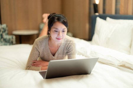 Mujer reloj en el ordenador portátil y acostado en la cama en casa