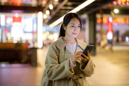 Téléchargez les photos : Femme d'affaires regarder le téléphone mobile dans la ville la nuit - en image libre de droit