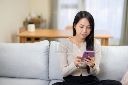 Photo for Woman look at mobile phone and sit on sofa at home - Royalty Free Image