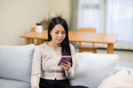 Foto de Mujer mira el teléfono móvil y sentarse en el sofá en casa - Imagen libre de derechos